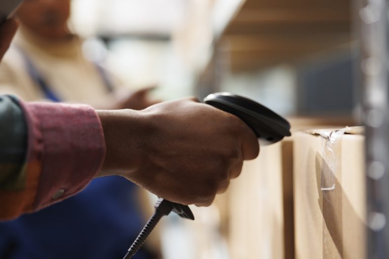 Operador logístico escaneia caixa em estoque de micro fulfillment, agilizando a separação de pedidos para o e-commerce.