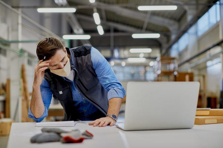 Profissional em armazém analisando documentos com expressão de preocupação, ao lado de um laptop, representando desafios e problemas logísticos na operação.